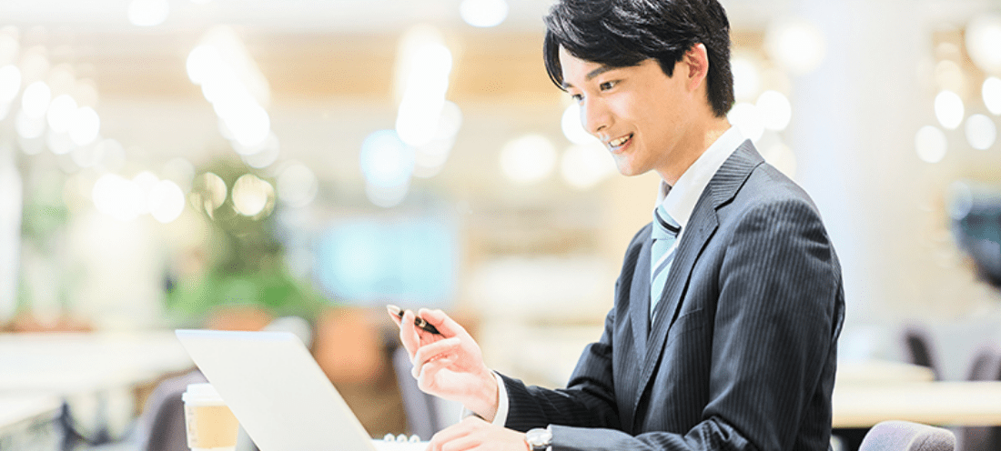 ノートパソコンで作業を進めている笑顔のスーツ姿の男性